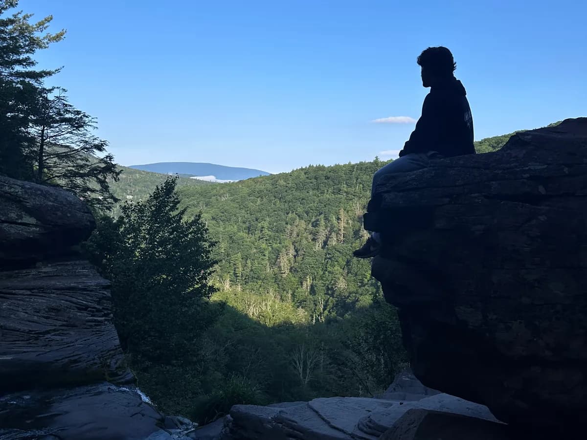 Burak sitting on a rock ledge above a forested valley.
